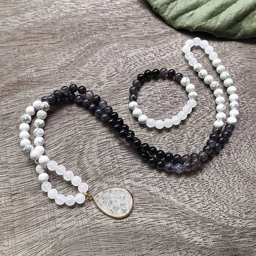 Ascendancy Gems Awakening Mala Set: 108-bead necklace & bracelet with white howlite, black onyx, and quartz beads. Features a teardrop quartz pendant.