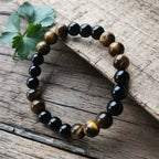 Ascendancy Gems handcrafted bracelet with alternating natural black onyx and tiger eye beads on a rustic wood surface.