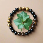 Ascendancy Gems beaded bracelet with alternating black onyx and tiger eye gemstones surrounding a green leaf.