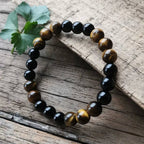 Ascendancy Gems beaded bracelet featuring alternating natural black onyx and tiger eye stones on a rustic wood surface.