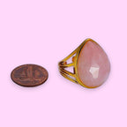 Ascendancy Gems gold-filled ring with a large, multifaceted teardrop-shaped pink gemstone. The band has a unique open cage design.