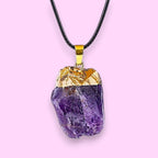 Ascendancy Gems raw amethyst crystal pendant necklace with gold cap and black cord.