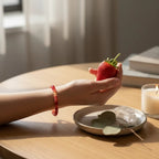 Ascendancy Gems red Ethiopian fire opal beaded bracelet worn on a hand holding a fresh strawberry on a wooden table.